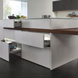 Vom Sockel geholt   Bisher gehörte er immer mit zur Küchenfront dazu: der Sockel. Jenes leicht nach hinten versetzte Ding, auf dem die Küchenschränke stehen. Nun ist er weg, jedenfalls bei einigen Designerküchen. Die Schranktüren sind bis nach unten durchgezogen und lassen den Sockel damit verschwinden. Es entsteht eine massive Küchenfront, die nun viel mehr nach edler Einrichtung als nach funktionaler Küche ausschaut. Dazu passt auch der Trend zur "grifflosen" Küche, bei der dezente Griffschienen oder Leisten die alten Knöpfe und Bügel ersetzen.