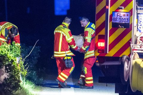 Zwei Männer in Feuerwehr-Kleidung tragen einen in Papier gehüllten, fußballgroßen Stein von der Unfallstelle auf der A7