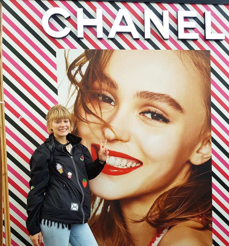 Mädchen in Regenjacke macht Peace-Zeichen vor Chanel-Plakat