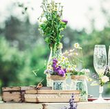 Weniger ist mehr!  Opulente Blumensträuße und Gestecke sind schön – aber längst nicht immer nötig, wenn es um einen schönen oder gar edel gedeckten Tisch geht. Der Trick: Anstelle von großen Sträußen, einfach mal zu einzelnen Schnittblumen, zum Beispiel Ranunkeln, Tulpen, oder Rosen greifen und diese in unterschiedlich großen Portionen in verschiedenen Vasen, Flaschen und Gläsern auf dem Tisch dekorieren. Das Ganze lebt von kleinen, aber feinen Unterschieden: Immer etwas höhere mit etwas niedrigeren Schnittblumen, sowie etwas feinem und gröberem Grün mischen. Nichts binden, sondern einfach locker in unterschiedlich großen und verschieden geformten Vasen fallen lassen. Je nach Jahreszeit immer mal wieder bei den Farben und Blumen ganz nach persönlichem Gusto und passend zum Anlass variieren. So entsteht im Nu ein kleiner, wilder – oder auch weniger wilder! – Bauerngarten im Glas!