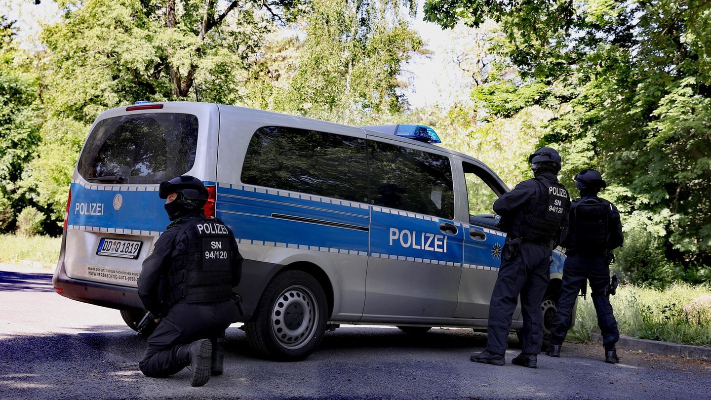 Drei Polizisten stehen mit Helmen und Sturmhauben auf an einem silber-blauen Transporter der Polizei