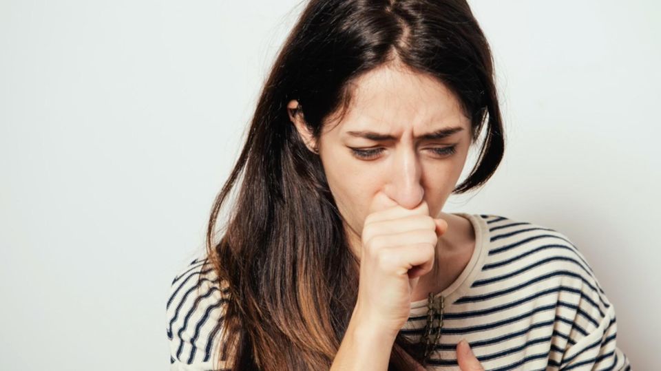 Frau hustet und hält sich die Hand vor den Mund