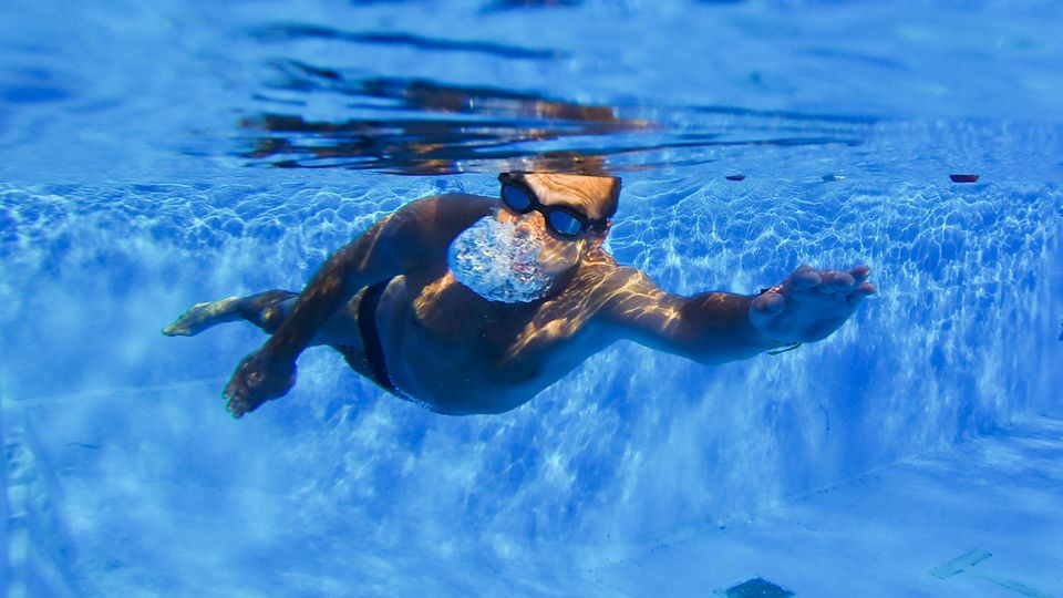 Ein Mann schwimmt in einem Schwimmbecken, fotografiert aus der Unterwasser-Perspektive Schon schlecht, wenn der 1. Mai oder der 3. Oktober auf einen Sonntag fallen, an dem man ohnehin frei hat. Die Linke hat eine Idee, wie man dieses Dilemma lösen könnte.
