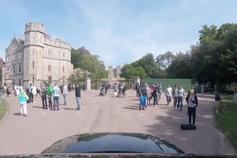 Vor der Einfahrt zu Schloss Windsor stehen Touristengruppen. Am unteren Bildrand ist die schwarze Motorhaube des Autos zu sehen