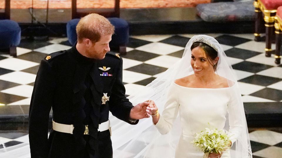 Hand in Hand schreiten Prinz Harry und Meghan Markle als Ehepaar durch die Kirche in Windsor. Sie lächelt ihn an.