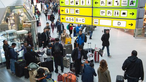Mehrere Menschen warten an einem Flughafen mit ihren Koffern