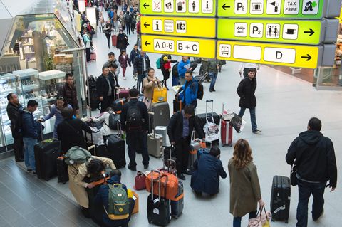 Mehrere Menschen warten an einem Flughafen mit ihren Koffern