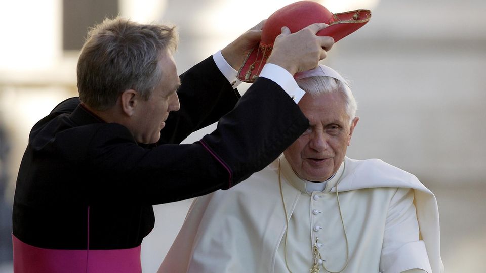 Noch immer sorgt sich Gänswein als Sekretär um Papst emeritus Benedikt. Als der noch im Amt war, setzte sein "Mitarbeiter" ihm auch mal einen roten Cappello Saturno über den weißen Zucchetto