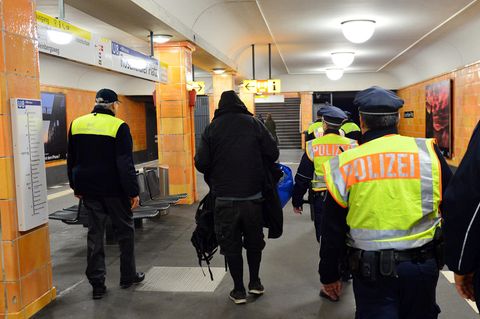 Mehrere Polizisten in Westen begleiten einen schwarz gekleideten Mann