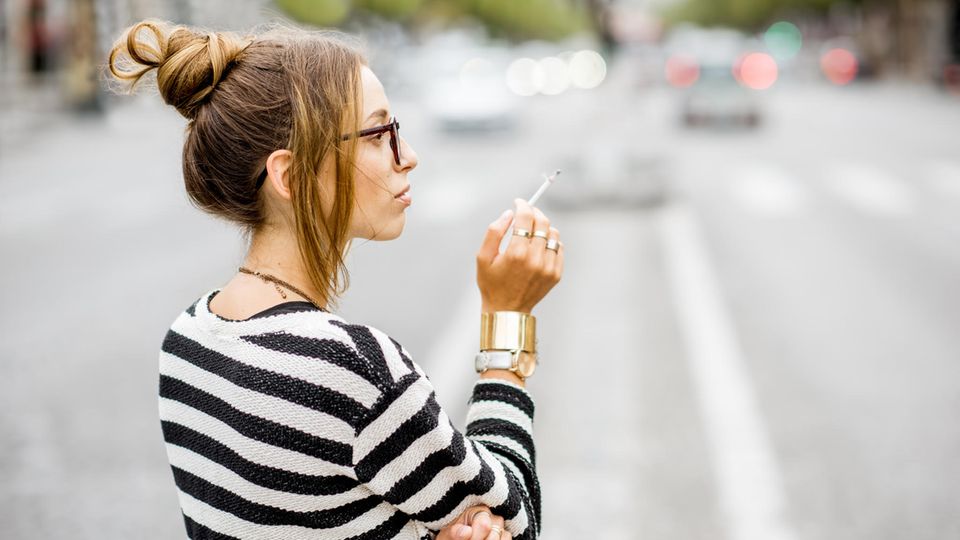 Eine junge Frau raucht auf der Straße eine Zigarette