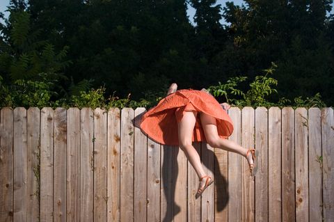 FOMO: Eine Frau hängt über einem Zaun, um auf die andere Seite zu schauen