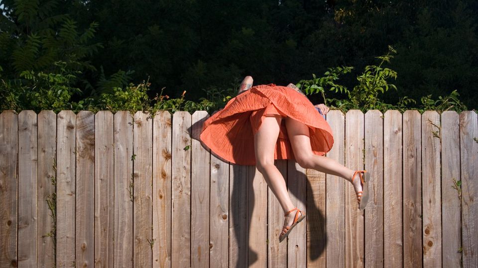 FOMO: Eine Frau hängt über einem Zaun, um auf die andere Seite zu schauen