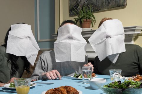 Drei junge Menschen essen an einem Tisch und haben Servietten vor ihren Mündern