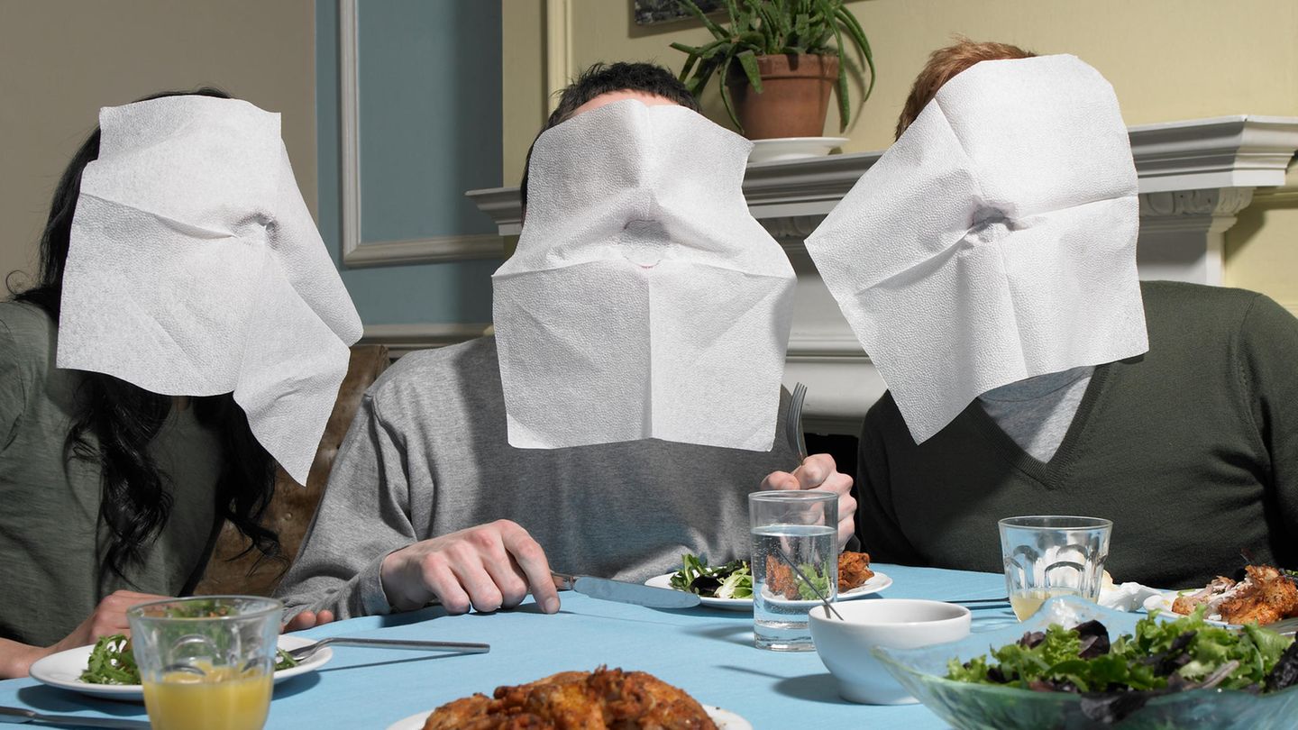 Drei junge Menschen essen an einem Tisch und haben Servietten vor ihren Mündern