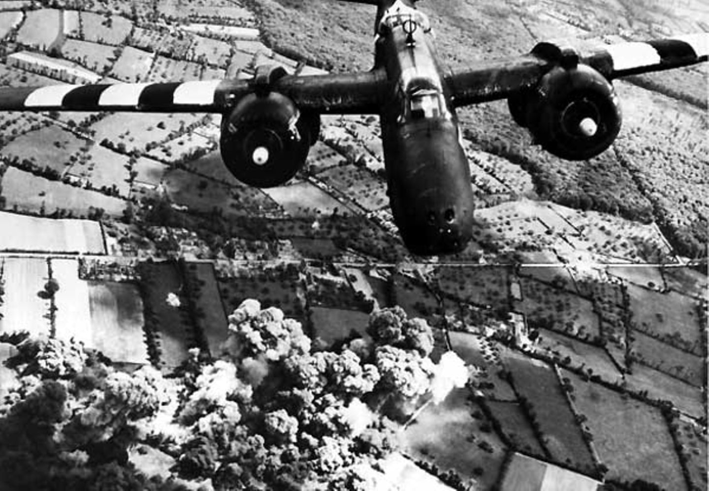 Bombenangriff  Ein zweimotoriges amerikanisches Kampfflugzeug vom Typ A-20 Havoc greift in der Region Cotentin Stellungen und Nachschubwege der Wehrmacht an. Am Boden steigen Wolken vorangegangener Explosionen auf.