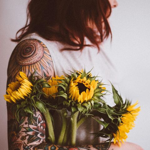 Eine tättowierte Frau hält Blumen im Arm