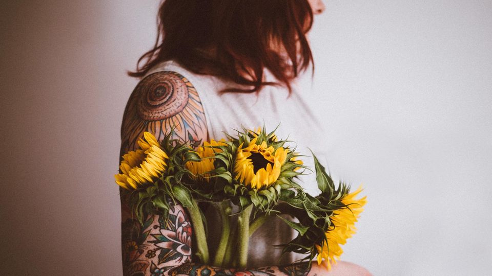 Eine tättowierte Frau hält Blumen im Arm