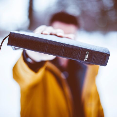 Ein junger Mann hält sich eine Bibel vor das Gesicht