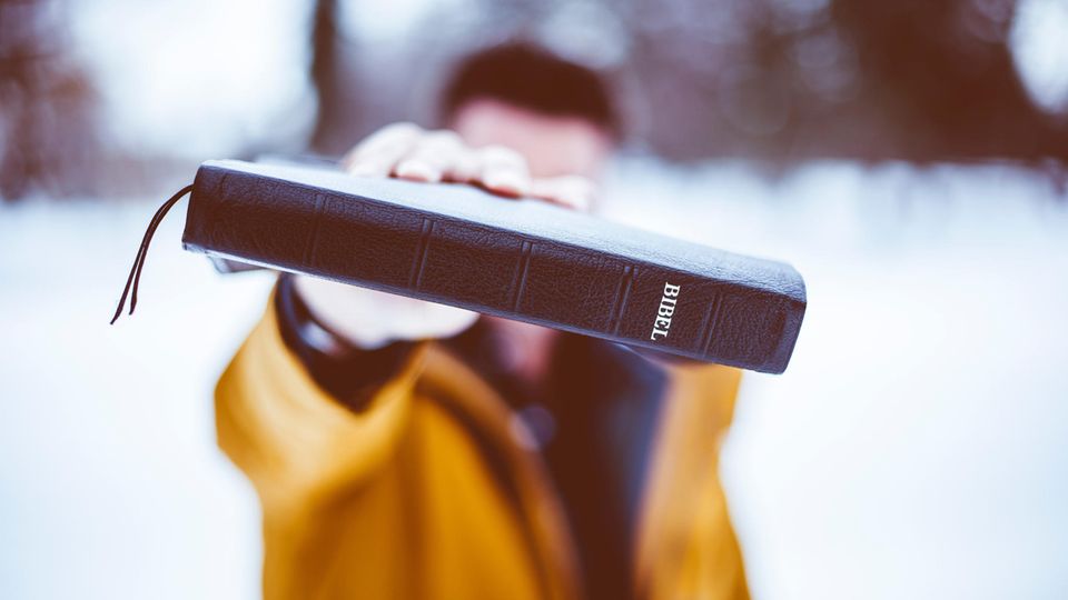 Ein junger Mann hält sich eine Bibel vor das Gesicht