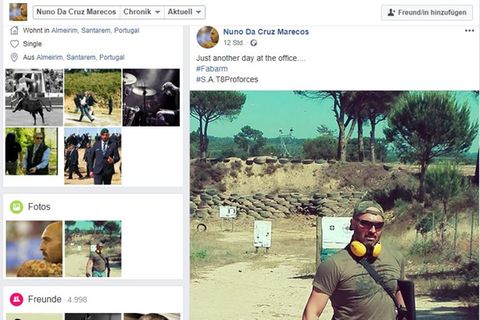 Ein muskulöser Mann mit Sonnenbrille und Ohrschützern posiert mit einem schweren Gewehr auf einem Schießplatz