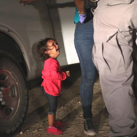Ein kleines Mädchen aus Honduras sieht weinend zu, seine Mutter von einer texanischen Grenzbeamtin durchsucht wird
