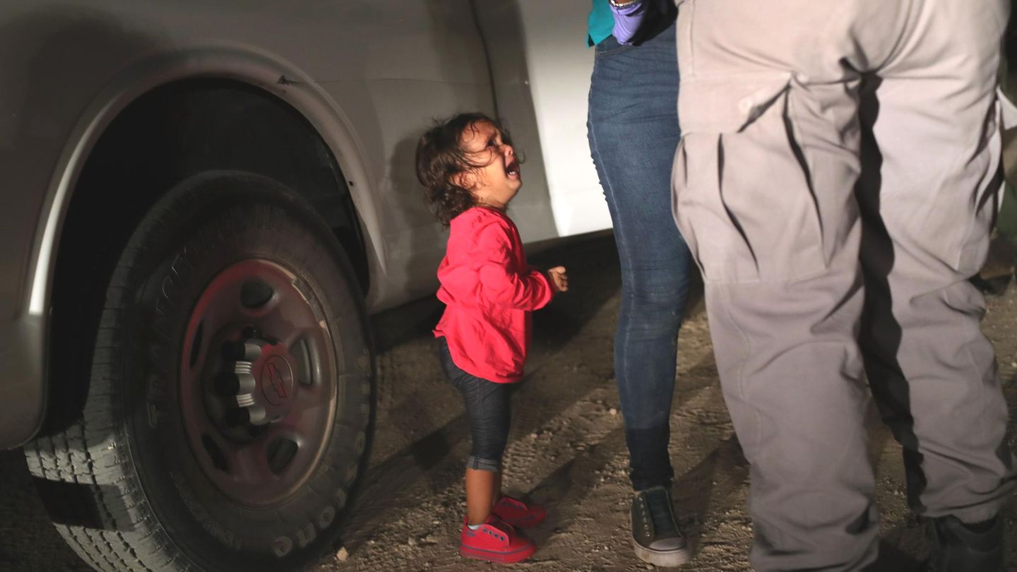 Ein kleines Mädchen aus Honduras sieht weinend zu, seine Mutter von einer texanischen Grenzbeamtin durchsucht wird