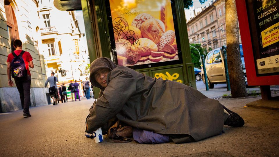 Ein obdachloser Bettler vor einem Werbeschild
