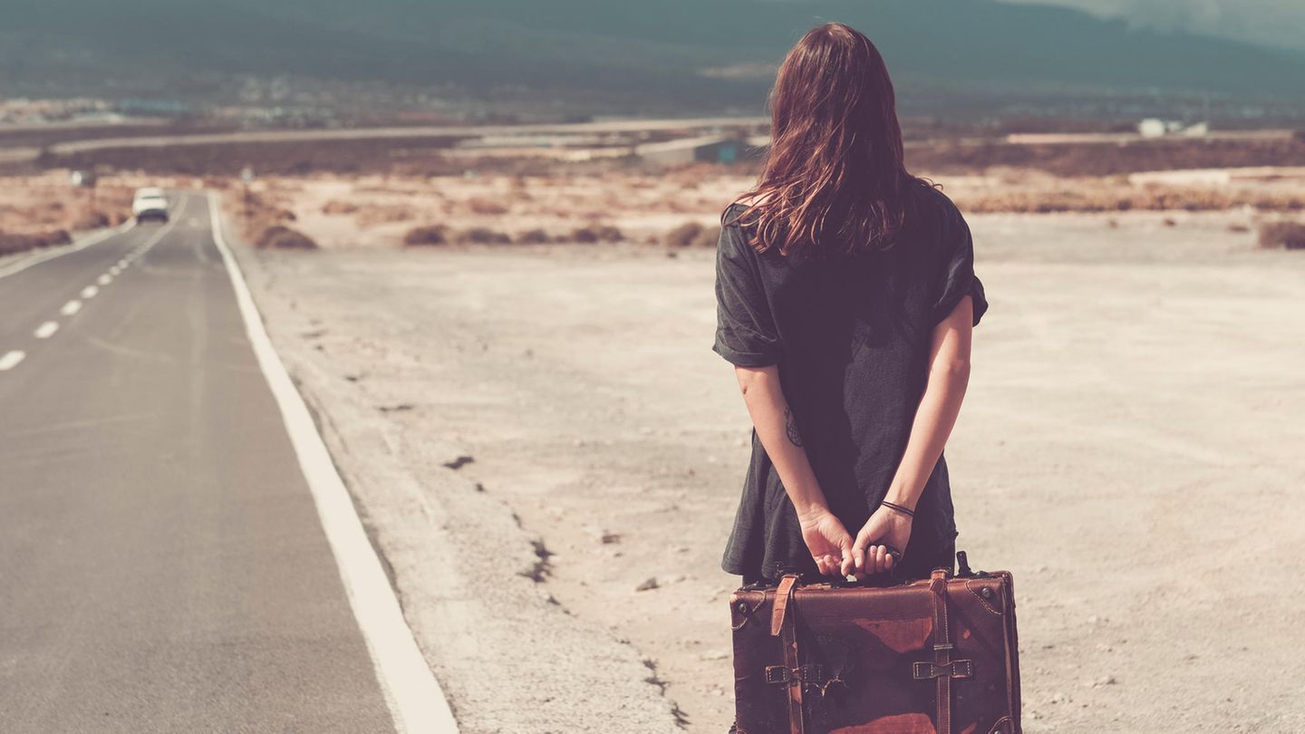 Eine Frau steht mit Koffer am Straßenrand