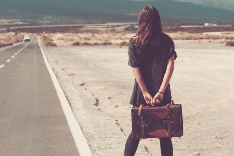 Eine Frau steht mit Koffer am Straßenrand