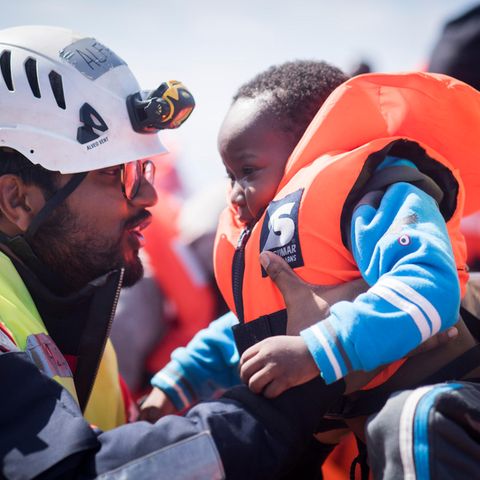 Ein "Sea-Watch"-Mitarbeiter hilft einem Kleinkind im Mittelmeer
