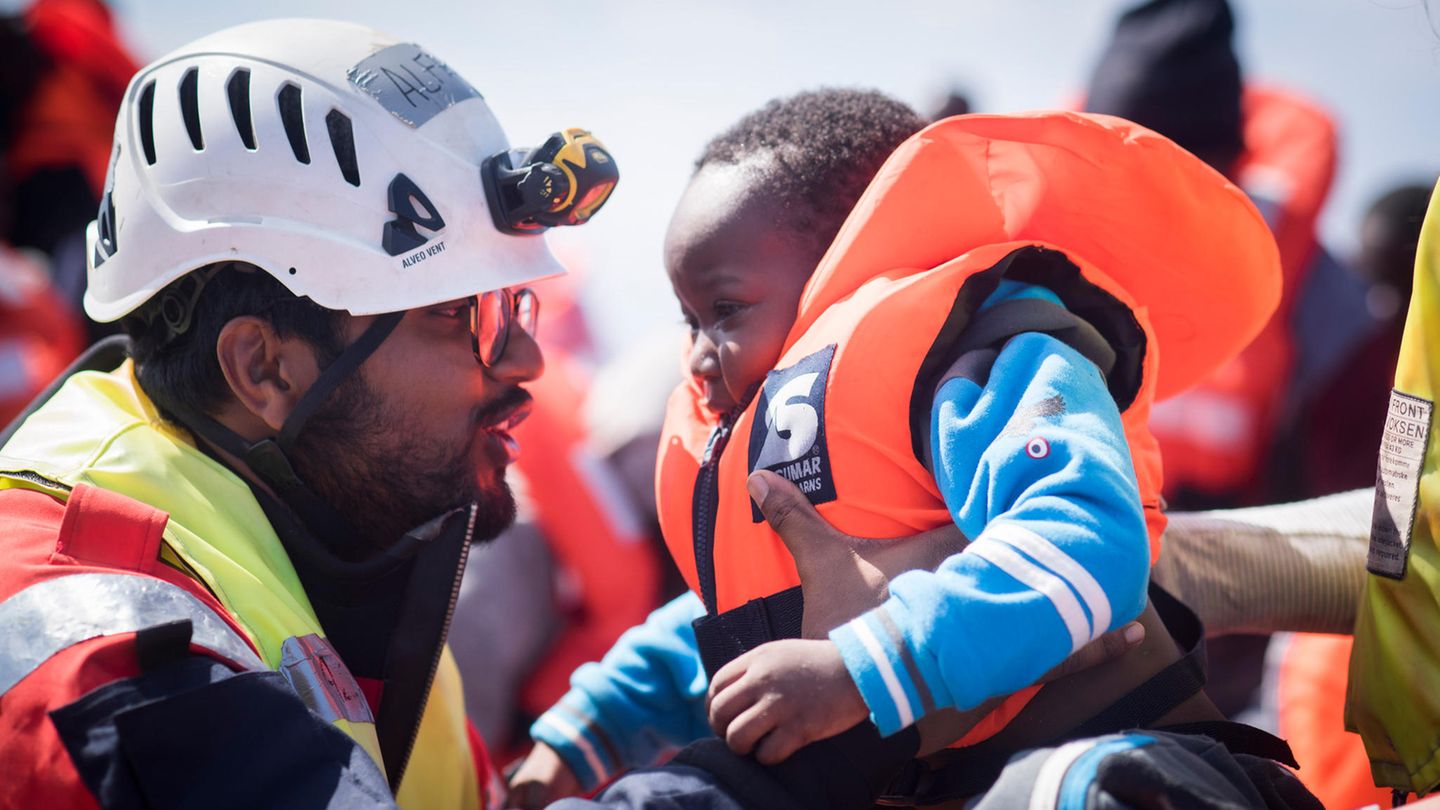 Ein "Sea-Watch"-Mitarbeiter hilft einem Kleinkind im Mittelmeer