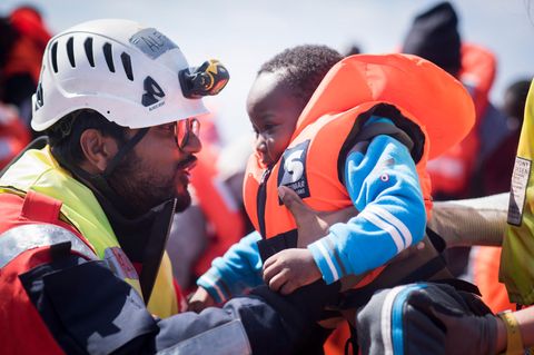 Ein "Sea-Watch"-Mitarbeiter hilft einem Kleinkind im Mittelmeer