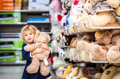 Kleines Mädchen mit Teddy-Bären im Arm am Supermarkt-Regal.