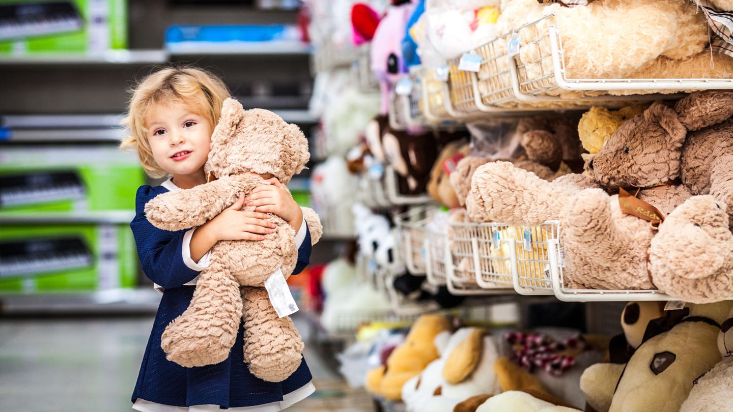 Kleines Mädchen mit Teddy-Bären im Arm am Supermarkt-Regal.