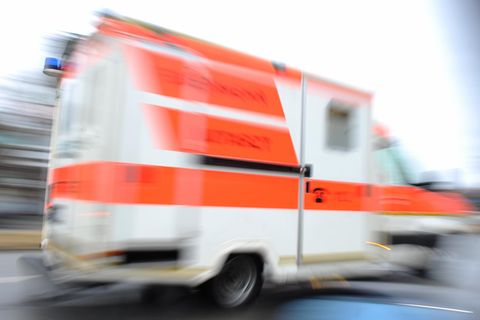 Ein weißer Krankenwagen mit orangenen Reflektorstreifen fährt schnell vorbei