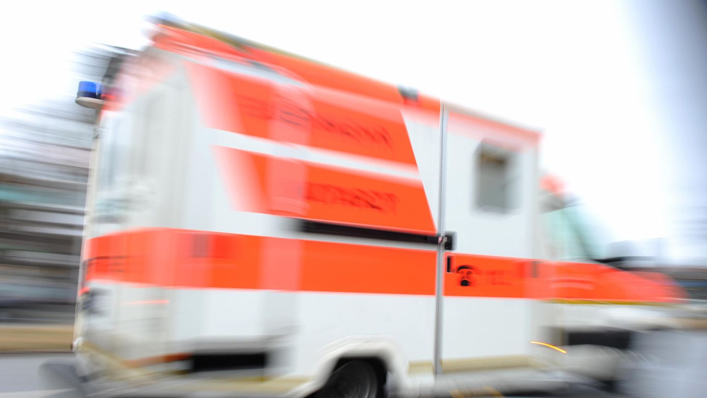 Ein weißer Krankenwagen mit orangenen Reflektorstreifen fährt schnell vorbei