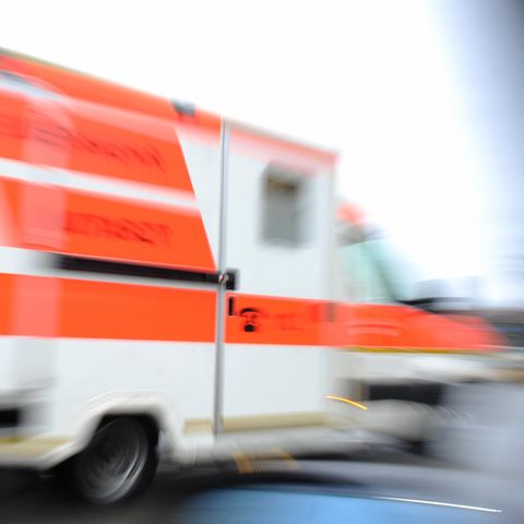 Ein weißer Krankenwagen mit orangenen Reflektorstreifen fährt schnell vorbei