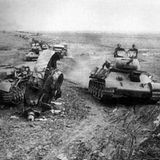 Eine Kolonne T-34 fährt an einem zerstörten Panzer IV vorbei.