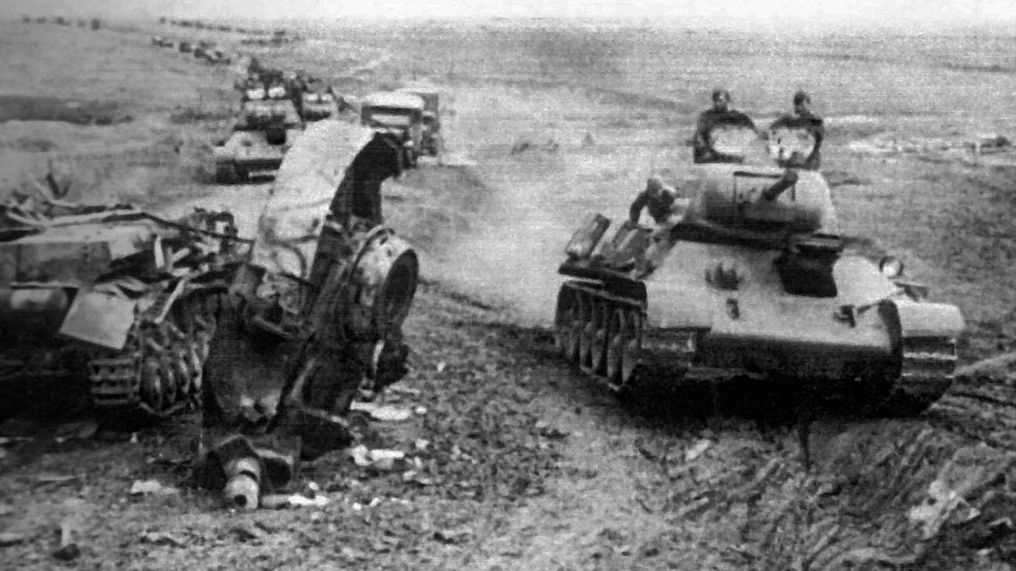 Eine Kolonne T-34 fährt an einem zerstörten Panzer IV vorbei.