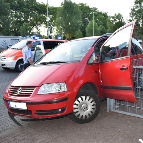 Ein roter VW hängt mit offener, nach vorne abgeknickter Fahrertür an der Ecke eines Metallzauns fest