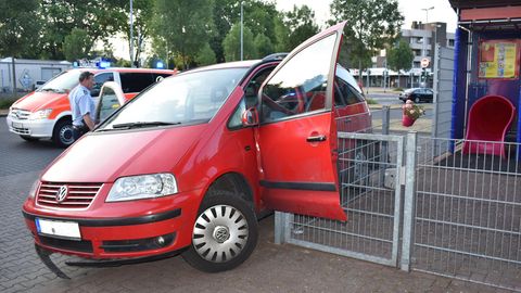 Ein roter VW hängt mit offener, nach vorne abgeknickter Fahrertür an der Ecke eines Metallzauns fest