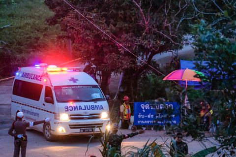 Ein weißer Krankenwagen mit Blau- und Rotlicht biegt ab, während behelmte Polizisten ihm den Weg weisen