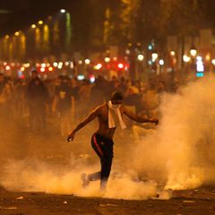 Frankreich, Paris: Ein Mann tritt eine von der Polizei geworfene Tränengasgranate während Ausschreitungen auf der Champs Elysees