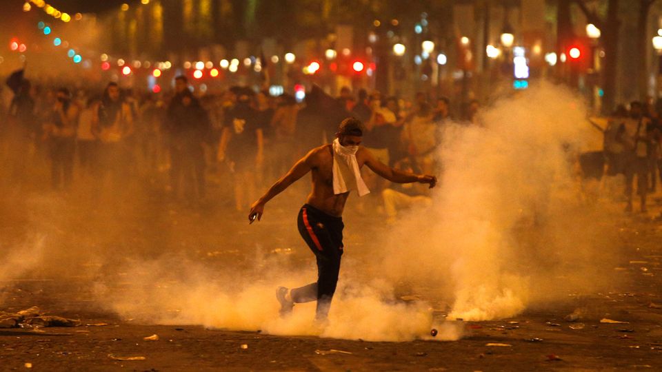 Frankreich, Paris: Ein Mann tritt eine von der Polizei geworfene Tränengasgranate während Ausschreitungen auf der Champs Elysees