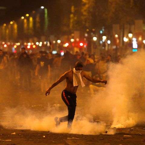 Frankreich, Paris: Ein Mann tritt eine von der Polizei geworfene Tränengasgranate während Ausschreitungen auf der Champs Elysees