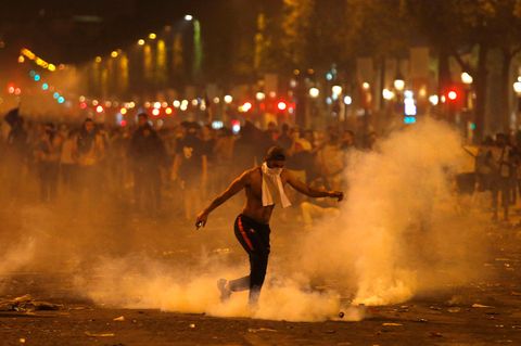Frankreich, Paris: Ein Mann tritt eine von der Polizei geworfene Tränengasgranate während Ausschreitungen auf der Champs Elysees