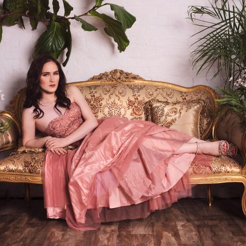 Abby Stein liegt in einem rosa Kleid auf einem Sofa.