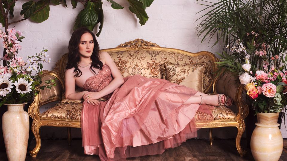 Abby Stein Abby Stein liegt in einem rosa Kleid auf einem Sofa.