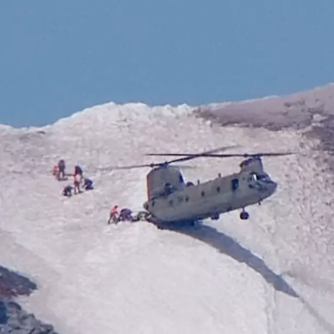 Ein Helikopter mit zwei Rotoren setzt mit einem Ende auf einem Hang auf, während die Schnauze in der Luft schwebt.
