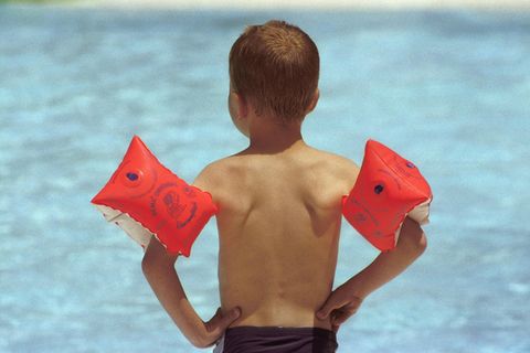 Ein Junge mit Schwimmflügeln steht im Schwimmbad